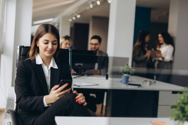 Arka planda office meslektaşları ile cep telefonu kullanarak gülümseyen iş kadını.