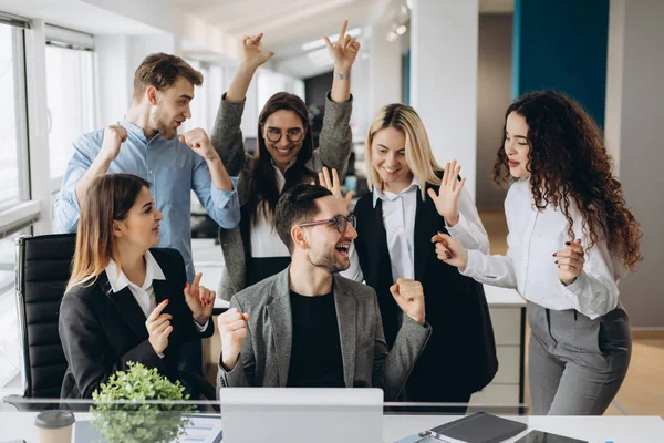 Male worker share good news with multiracial colleagues in shared workplace, diverse employees scream with happiness excited with corporate success or goal achievement, team celebrating win