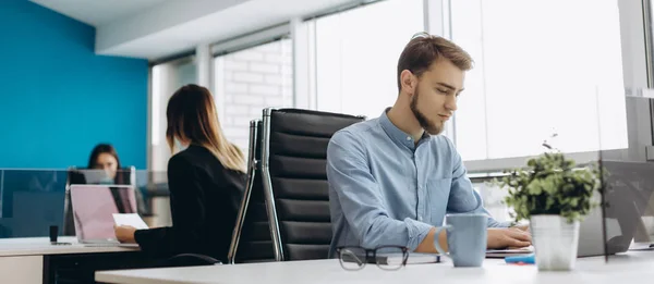 Full concentration at work. Handsome young beard man in shirt working on laptop while sitting at his working place