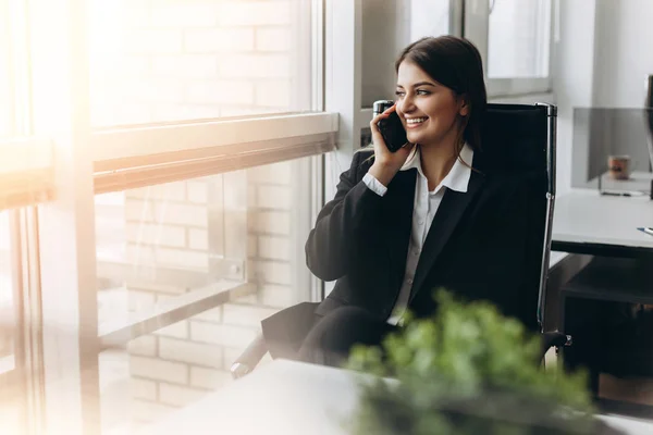 Sharing good business news. Attractive young woman talking on the mobile phone and smiling while sitting at her working place in office.