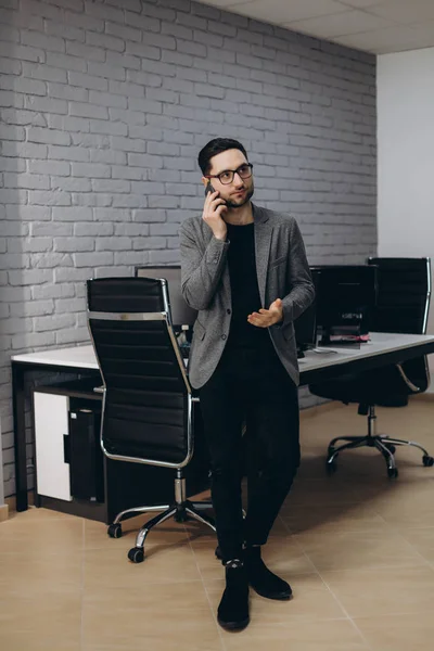 Attractive handsome young brunet bearded smiling executive worker man in office work station work place, talking on the phone