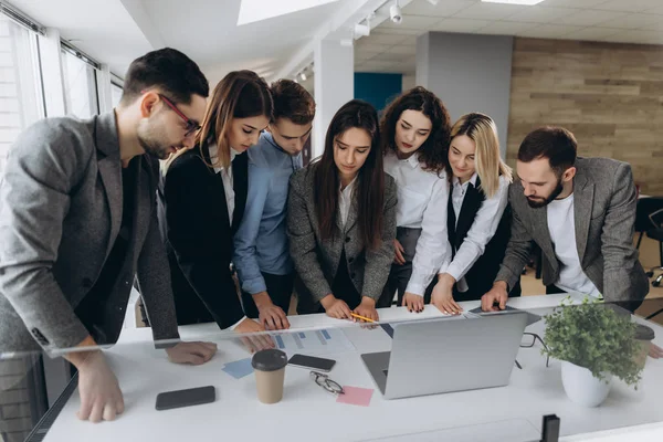 Concentración total en el trabajo. Grupo de jóvenes empresarios que trabajan y se comunican mientras están de pie en una oficina moderna . — Foto de Stock
