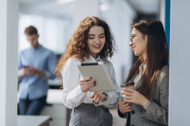 Ofis salonunda yürürken dijital tablet üzerindeki proje fikirlerini tartışan iki kadın yönetici, konferans salonuna giderken dokunmatik yüzey üzerinde çalışan kendine güvenen kadın girişimciler
