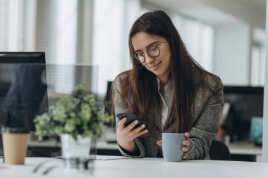 Young woman sitting in office and using phone