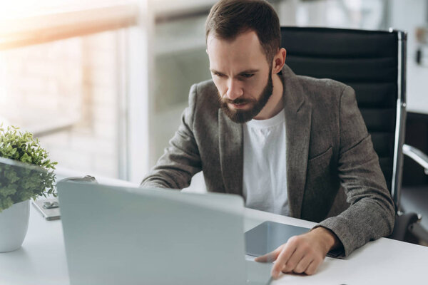 Bearded young businessman working at modern office.Man wearing white shirt and making notes on the documents.Panoramic windows background. Horizontal, film effect.Blurred