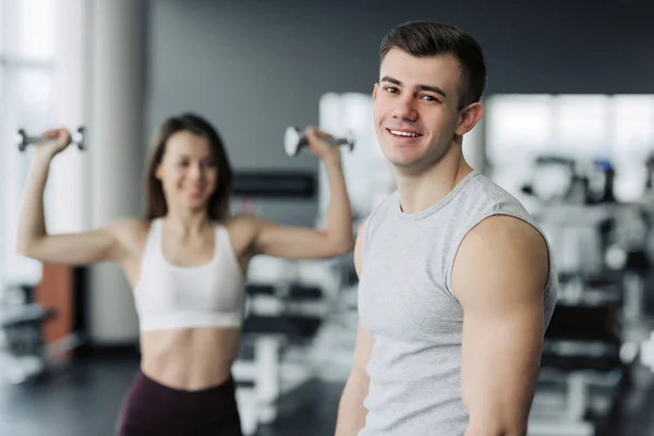 Result take effort. The athlete relaxing in the gym after strength exercises for different muscles, work out his body, push-up, squats and abs crunches with the training girl on background. Fitness, h — Stock Photo, Image