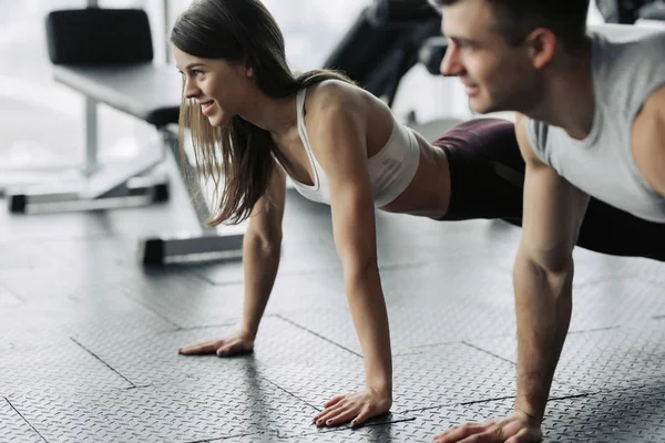 Genç çift spor salonunda çalışıyor. Çekici kadın ve yakışıklı kaslı adam modern spor salonunda antrenman yapıyorlar. Kalas yapıyorum. Şınav çekiyorum..