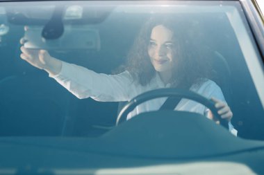 Dikiz aynasında sürücü. İş dünyasında çekici genç kadın dikiz aynası görünümlü ve bir araba sürerken gülümseyen giymek.