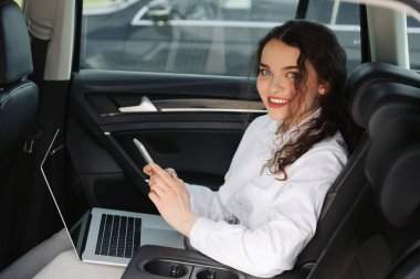 Arabada dizüstü bilgisayar ve telefon kullanarak güzel genç iş kadını.