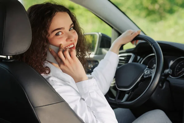 Back view of an attractive young business woman looking over her shoulder and talking the phone while driving a car.