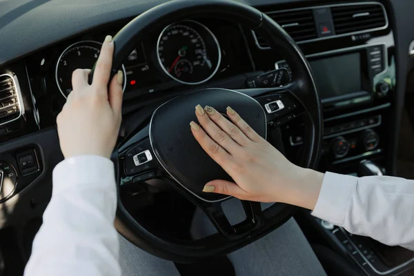 Close up of a women is hands holding a car\'s steering wheel and honking the horn.