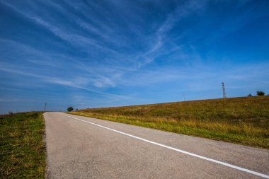 Yaz aylarında çim alanın üzerinde boş asfalt yol. Mavi gökyüzü beyaz bulutlar ile