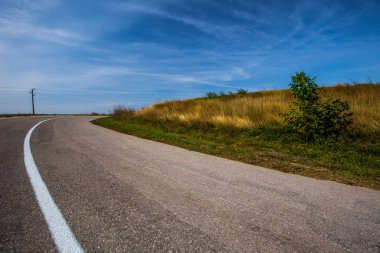 Sarı çim alan. Yaz aylarında boş asfalt yol üzerinde beyaz bulutlar ile mavi gökyüzü