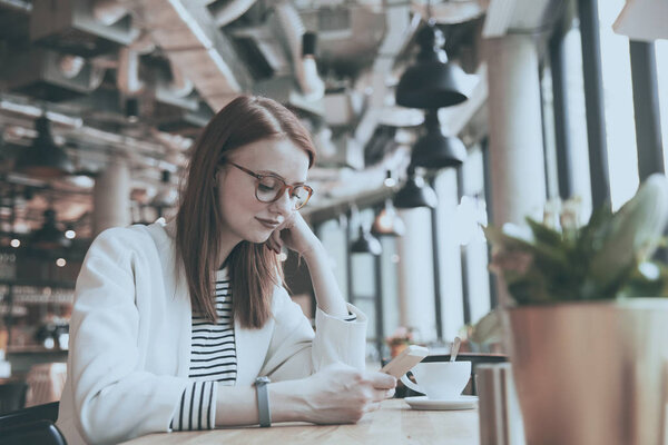 Молодая женщина сидит в кафе и использует смартфон
 