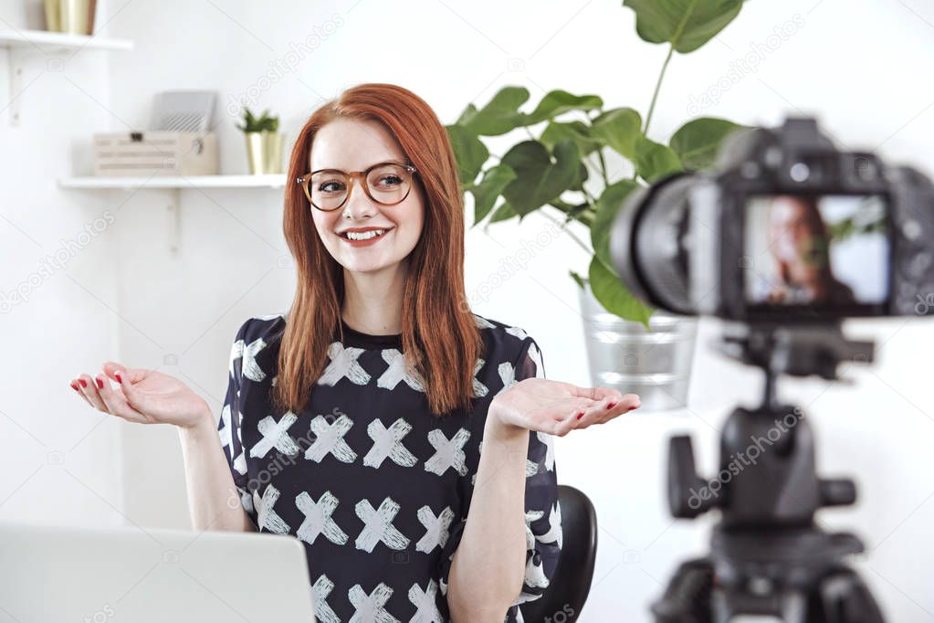 Cheerful young blogger filming video on digital camera at home