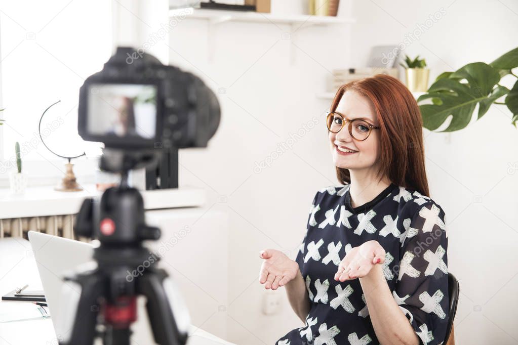 Cheerful young blogger filming video on digital camera at home