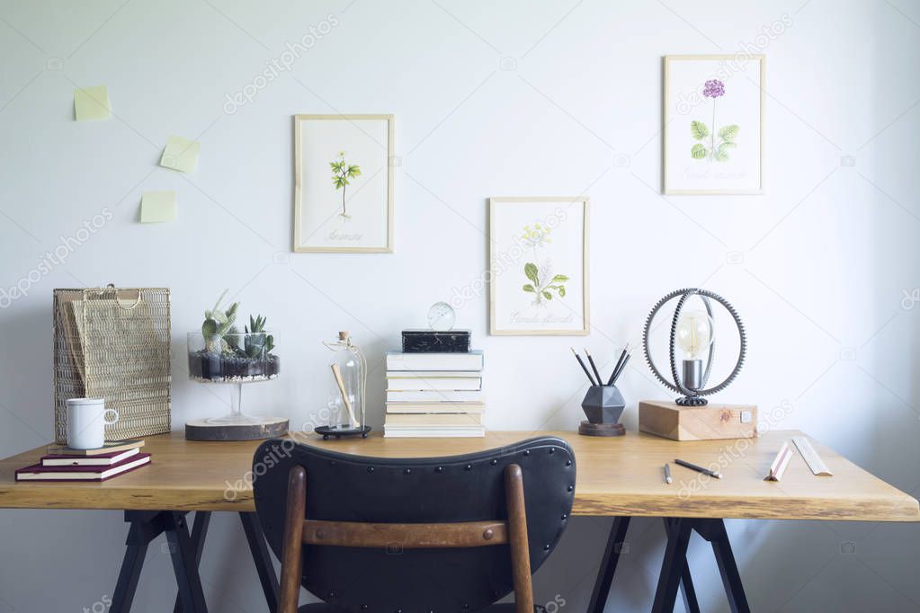 Vintage, creative home office interior with wooden desk, books, notebooks, romantic illustrations of plants, table lamp and office accessories. Stylish space for freelancer.