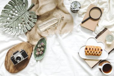 Dizüstü bilgisayar, kamera, pastel pembe makaronlar, beyaz çarşaf arka plan üzerinde kadın aksesuarları ile yatakta çalışma alanı Düz yatıyordu. Düz yatıyordu, üst görünüm blogger influencer ev ofis kavramı.