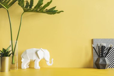Yapraklı sarı masa, fil figürü, bitki ve ofis aksesuarları. Sarı arka planlı yaratıcı alan. Uzayı kopyala İçişleri Bakanlığı.