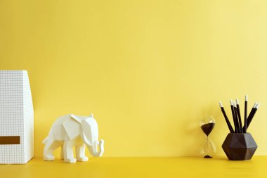 İçinde fil figürü, kum saati ve ofis aksesuarları olan sarı bir iç mekan. Sarı arka plan duvarlı yaratıcı alan. Ev dekorunun modern ve şık kompozisyonu. İçişleri Bakanlığı.