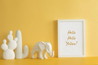 Fotoğraf çerçevesi ile kaktüsler ve fil figürü ile tasarım sarı masa. Modern mock up kavramı. Slogan için yer. Ev dekorasyonunun şık ve modern kompozisyonu. Ev ofis iç.