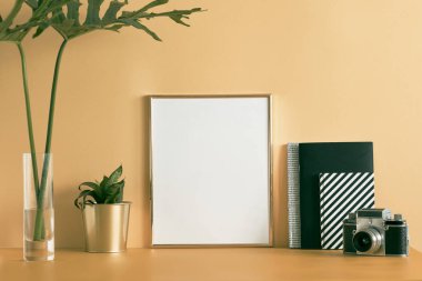Poster çerçevesi, kamera, bitki, tropikal yaprak ve dizüstü bilgisayarlar ile sahte yaratıcı masa. Modern ve minimalist masa konsepti. Ev dekorasyonunun şık ve modern kompozisyonu.