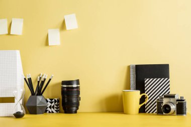 Yapraklar, bitki, ofis aksesuarları, yapışkan notlar ve retro fotoğraf makinesi ile Pastel sarı masa. Yaratıcı çalışma alanı. Kopya alanı. Şablon. Ev dekorasyonunun şık ve modern kompozisyonu.