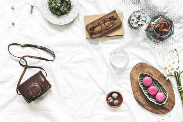 Flat lay of workspace in bed with notebook, camera, cup of coffee, woman accessories on white bedsheets background. Flat lay, top view blogger influencer home office concept.