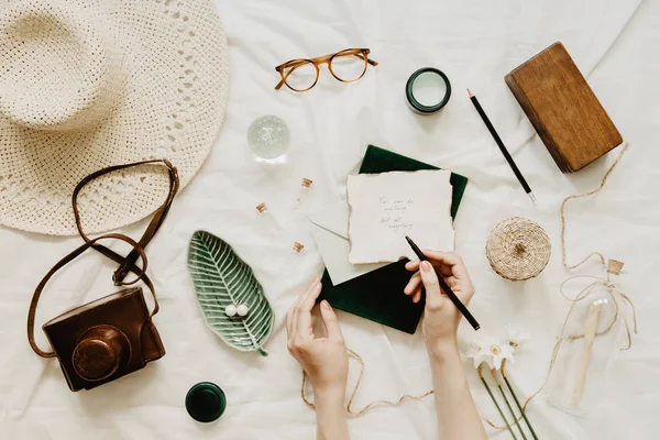 Trendy and stylish flat lay. Woman hands writting letters. Work space with accessories, hat, glasses, letters and notebook. Lifestyle and blogger concept.
