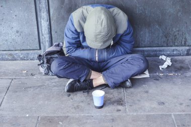 Homeless man sitting on pavement with cup for handouts clipart