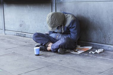 Homeless man sitting on pavement with cup for handouts clipart
