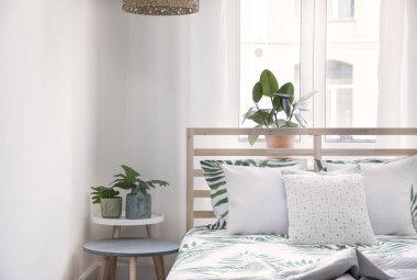 Bitkiler, çiçek desen yatak ve pilows ile şık ve modern İskandinav güneşli yatak odası. Beyaz duvarlar ve kahverengi ahşap parke ile alan. 