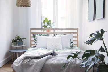 Bitkiler, çiçek desen yatak ve pilows ile Modern İskandinav güneşli yatak odası. Beyaz duvarlar ve kahverengi ahşap parke ile alan. 