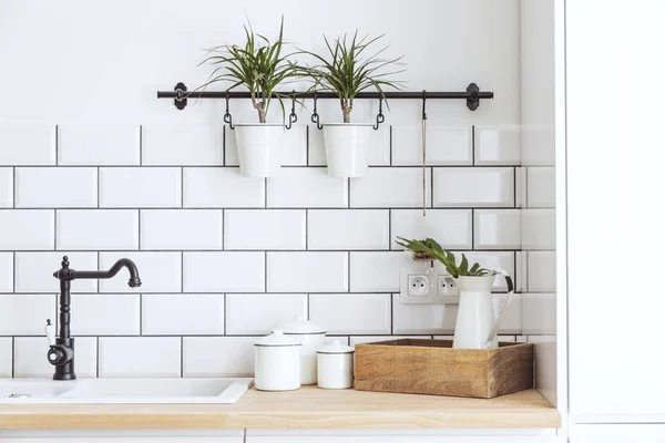 Modern and design scandinavian kitchen with plants, accessories and straw bag. Sunny and bright space with white brick wall.
