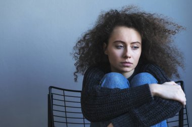 Depresif genç kıvırcık kadın sandalyede oturuyor