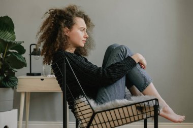 Depresif genç kıvırcık kadın sandalyede oturuyor