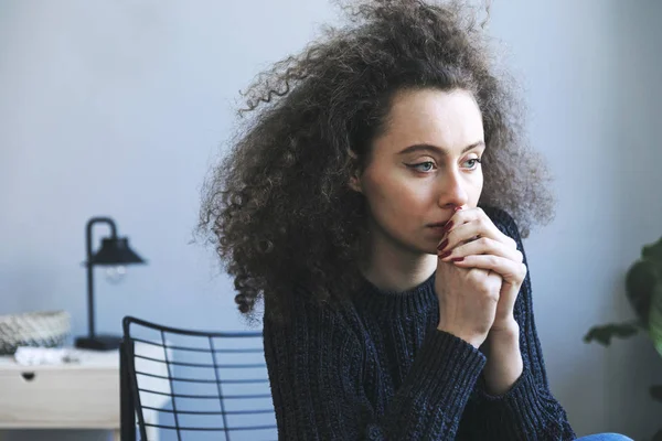 Depressed young curly woman sitting on chair