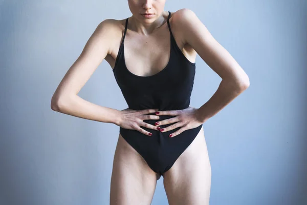 Young skinny woman in black maillot posing on grey background