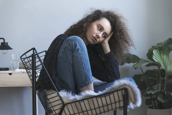 Depressed young curly woman sitting on chair