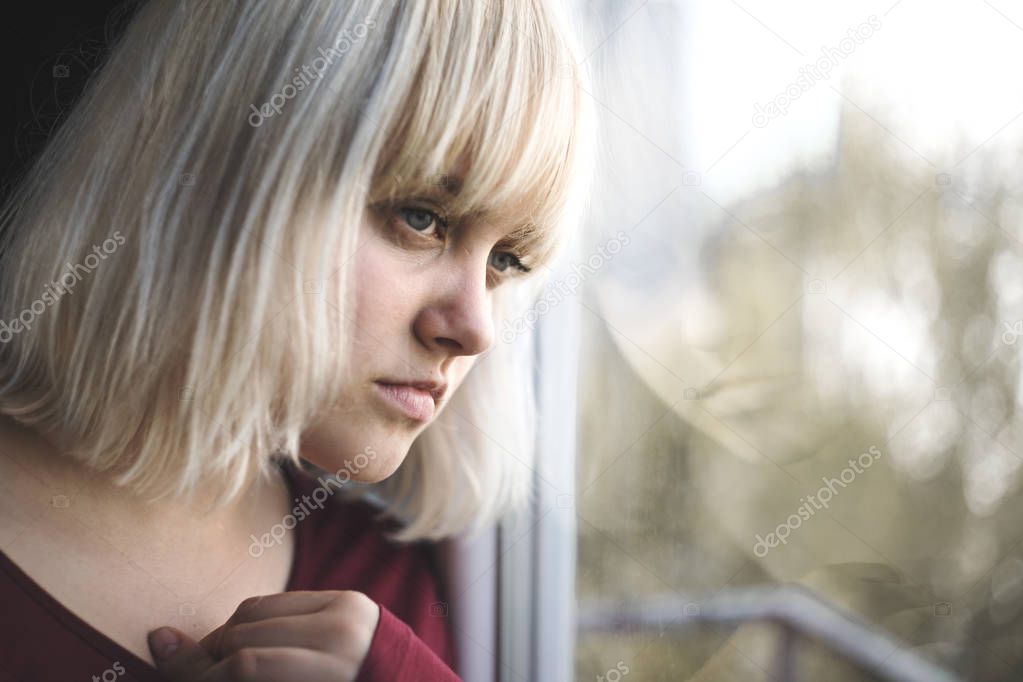 Portrait of sad depressed young woman sitting near window