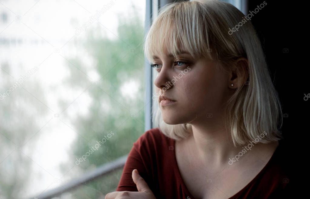 Portrait of sad depressed young woman sitting near window