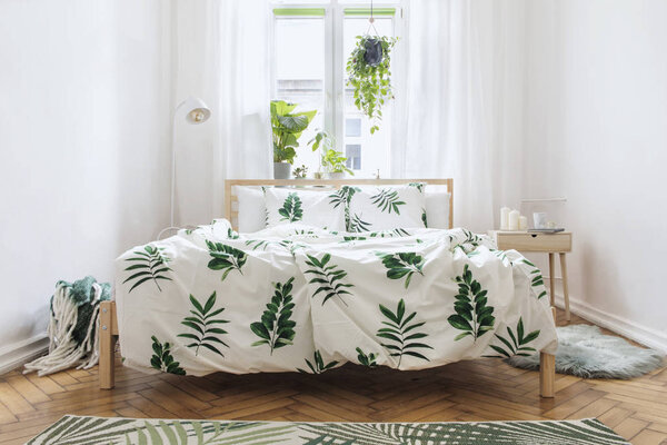 Light bedroom with wooden furniture, printed bed sheets and white linen blinds on window