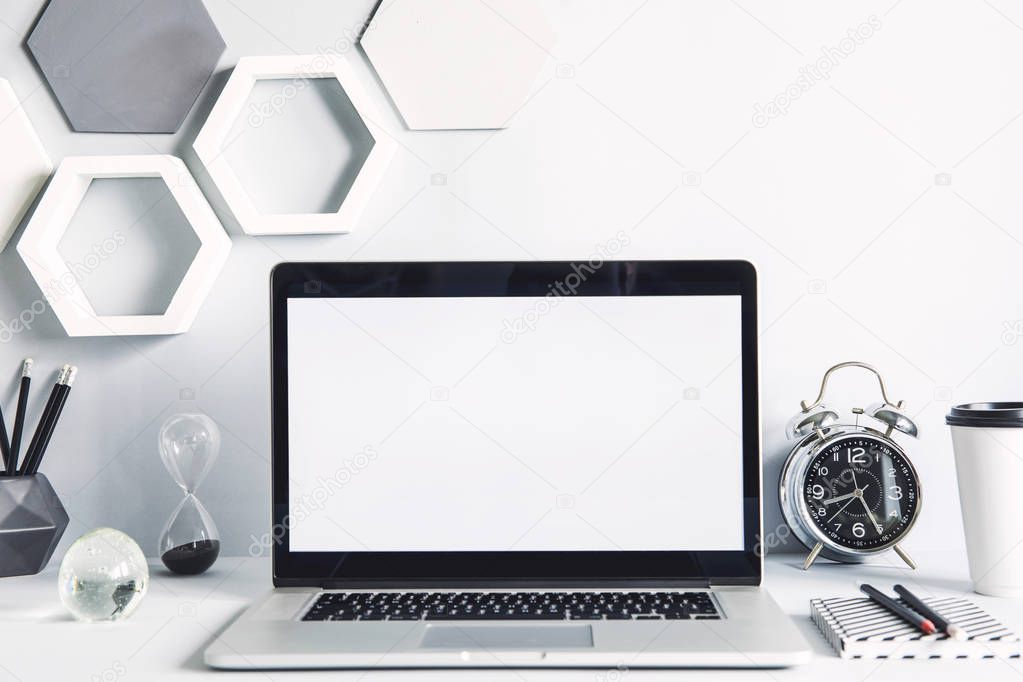 Modern work-space with laptop mock up screen and office accessories on white background with hexagon elements on wall