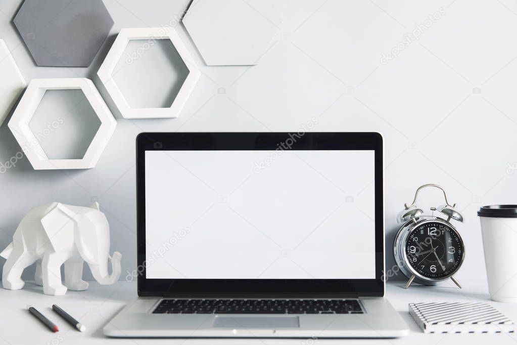 Modern work-space with laptop mock up screen and office accessories on white background with hexagon elements on wall