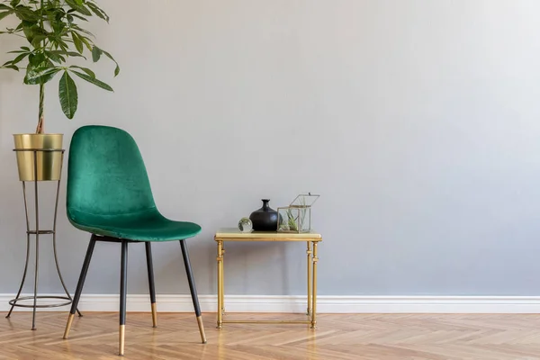 Luxury and minimalistic home interior with green velvet chair, coffee table with design accessories and plant in gold pot. Copy space for inscription, mock up poster. Brown wooden parquet.