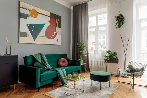 Stylish living room with green velvet sofa and abstract art on wall