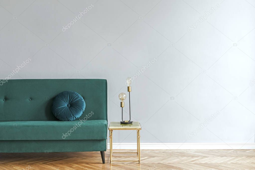 Minimalistic and luxury grey home interior with green velvet design sofa, gold coffe table with table lamp. Copy space for inscription, mock up poster. Empty wall. Brown wooden parquet.