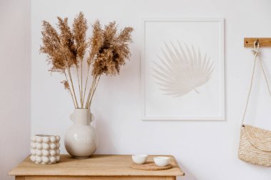 Kahverengi sahte poster çerçevesi, zarif aksesuarlar, vazo çiçekler, ahşap raf ve asılı Rattan çanta ile oturma odası şık Koreli iç. Ev dekoru Minimalistic kavramı. Şablon. Dekor.