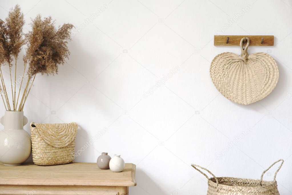 Stylish korean interior of living room with elegant accessories, flowers in vase, wooden shelf, basket and hanging rattan leaf. Minimalistic concept of home decor. Template. Copy space. Bright.