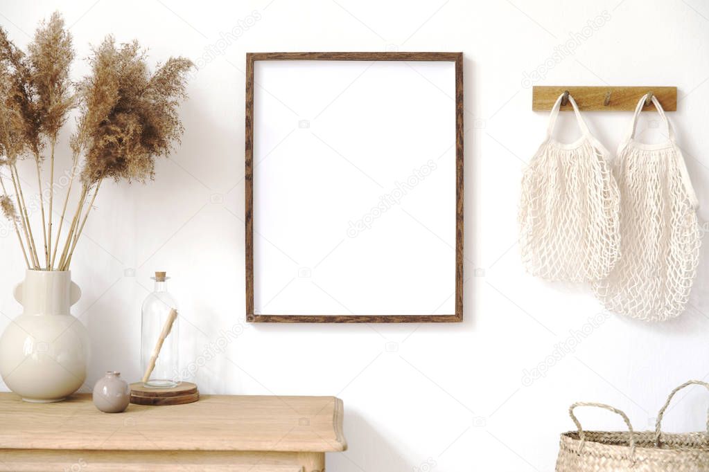 Stylish korean interior of living room with brown mock up poster frame, elegant accessories, flowers, wooden shelf and hanging rattan bags. Minimalistic concept of home decor. Template. Bright room.